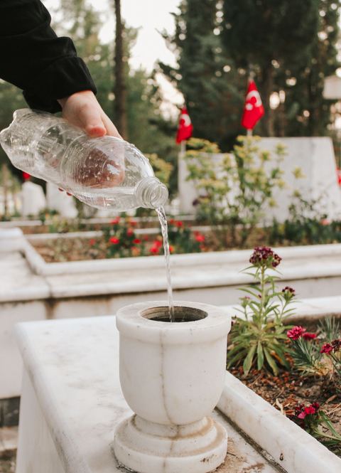 Une main verse de l'eau dans un pot de fleurs posé sur une sépulture